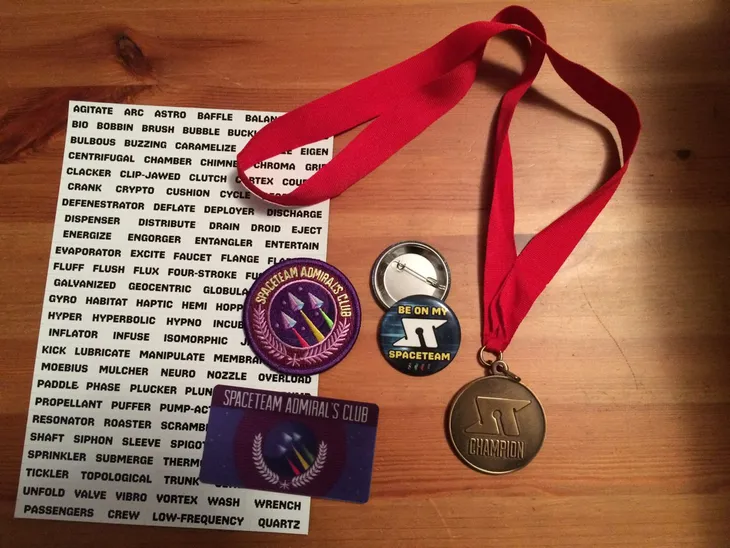 Admiral's Club swag on a table: a button, a medal, an embroidered patch, a lenticular 3D membership card, and a sheet of magnetic technobabble